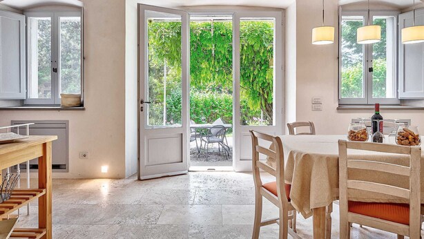 A spacious dining area with a large glass door leading to an outdoor garden, wooden furniture, and pendant lighting. - Villa Church with private pool - My Rental Homes (Cortona)