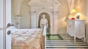 A bedroom with a bed, a dresser, a statue, and a staircase leading to another room. - Villa Church with private pool - My Rental Homes (Cortona)