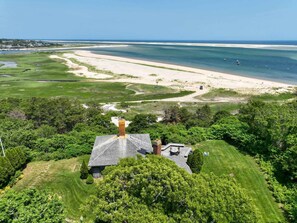 A house with a chimney, surrounded by lush greenery and a view of a beach and ocean. - Panoramic Water Views w/ Private Beach! (Chatham)