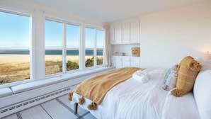 A bedroom with a large window, a bed, and a view of the beach. - Panoramic Water Views w/ Private Beach! (Chatham)