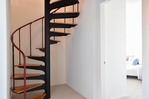 A spiral staircase with wooden steps and a red handrail, leading to a bedroom with a bed and a nightstand. - Panoramic Water Views w/ Private Beach! (Chatham)
