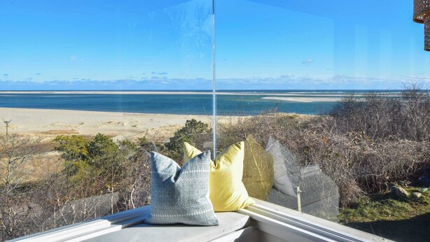 A window with a view of a beach and ocean, a railing, and some cushions. - Panoramic Water Views w/ Private Beach! (Chatham)