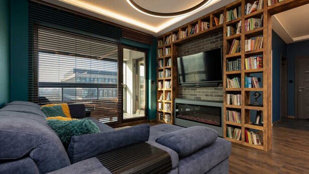 A modern living room with a sectional sofa, a fireplace, a TV, and a bookshelf.