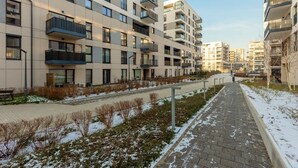 A modern apartment building with multiple balconies, a paved walkway, and snow on the ground.