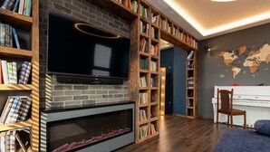 A cozy living room with a fireplace, bookshelves, a television, and a piano.