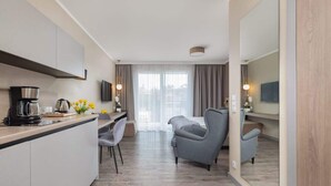 Une chambre d’hôtel moderne équipée d’une cuisine, d’un coin repas, d’un fauteuil gris et d’un grand miroir.