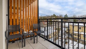 Un balcon avec deux chaises et une table, une cloison en bois et une vue sur un quartier enneigé.