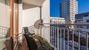Un balcón con vista a un edificio alto, una zona pavimentada y un camión estacionado.