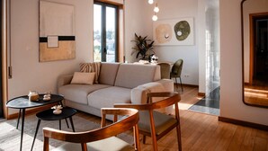 A modern living room with a sofa, chairs, a small table, and a dining area. - Stunning balcony with views of Tagus River, ocean and historic sites of Belém✨ (Lisboa)