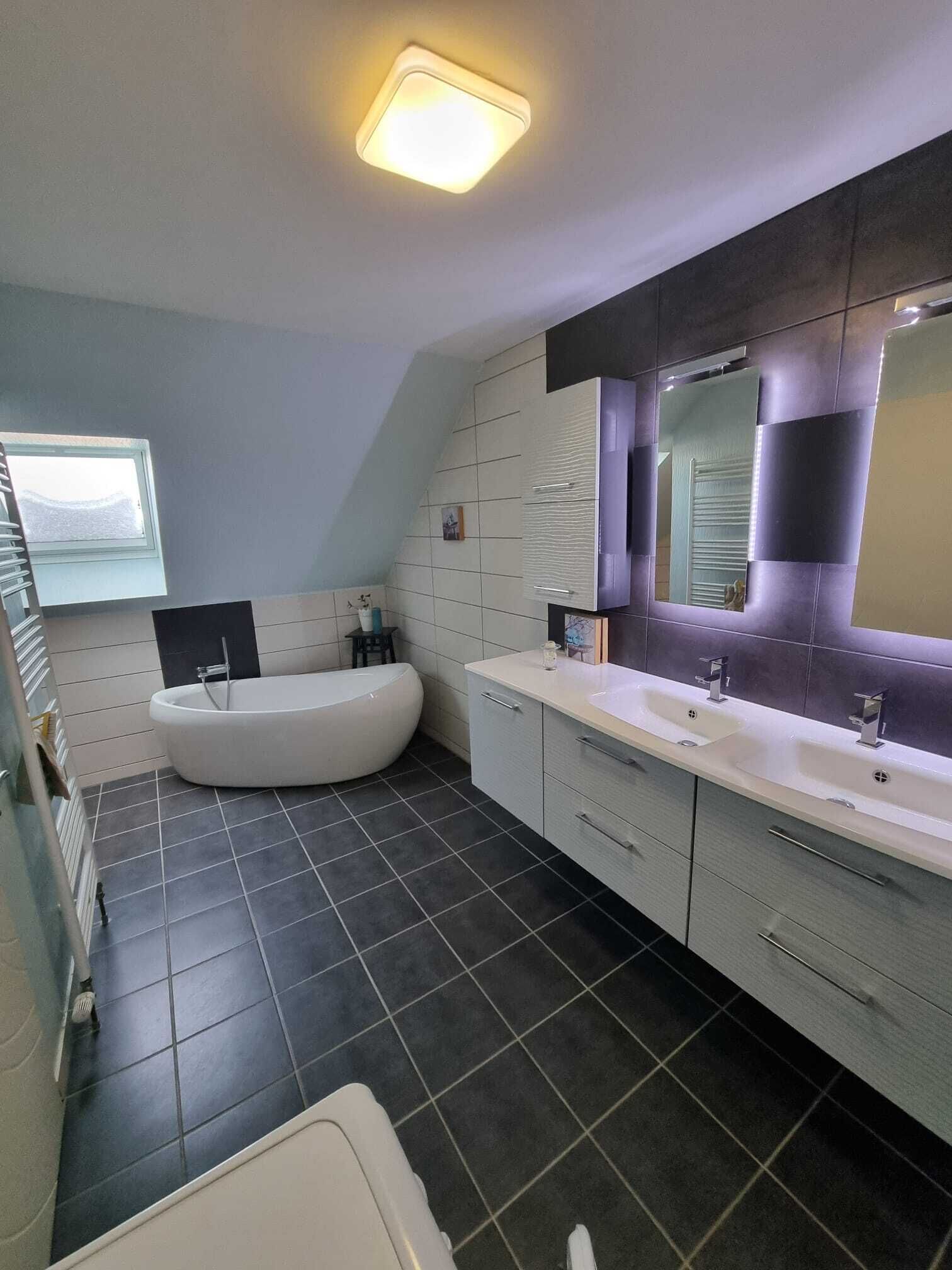 Un baño moderno con una bañera independiente, dos lavamanos y un espejo grande.