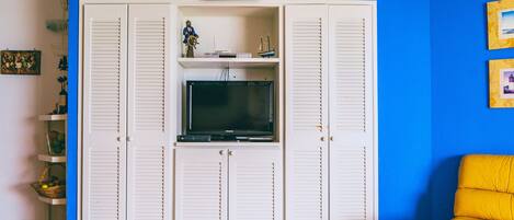A room with a blue wall, a white entertainment unit with a television, and a yellow sofa.