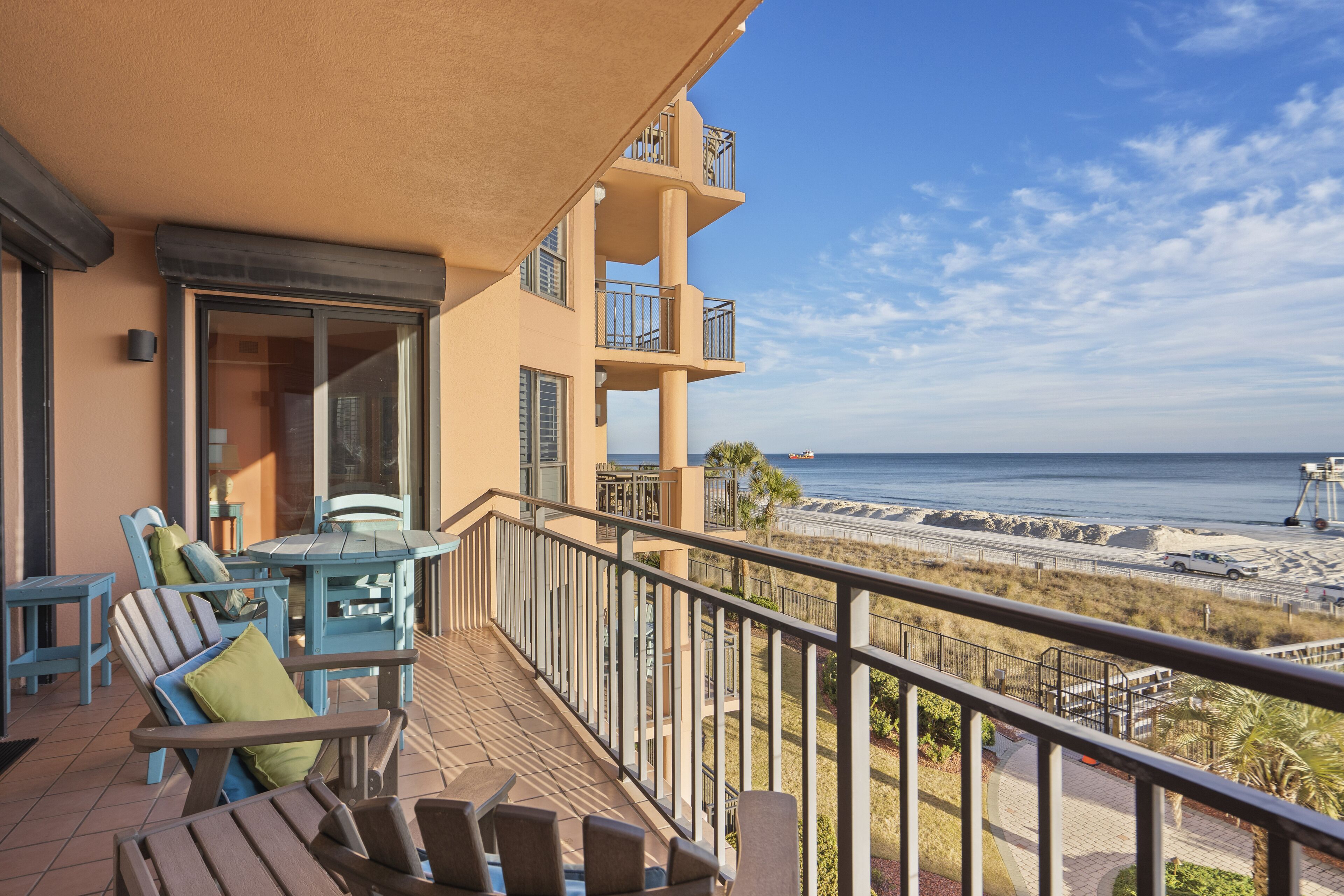 A balcony with outdoor furniture, a view of the beach, and a building with multiple balconies.