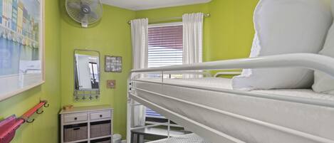 A bunk bed room with a fan, a window with curtains, a mirror, and a small cabinet with baskets.