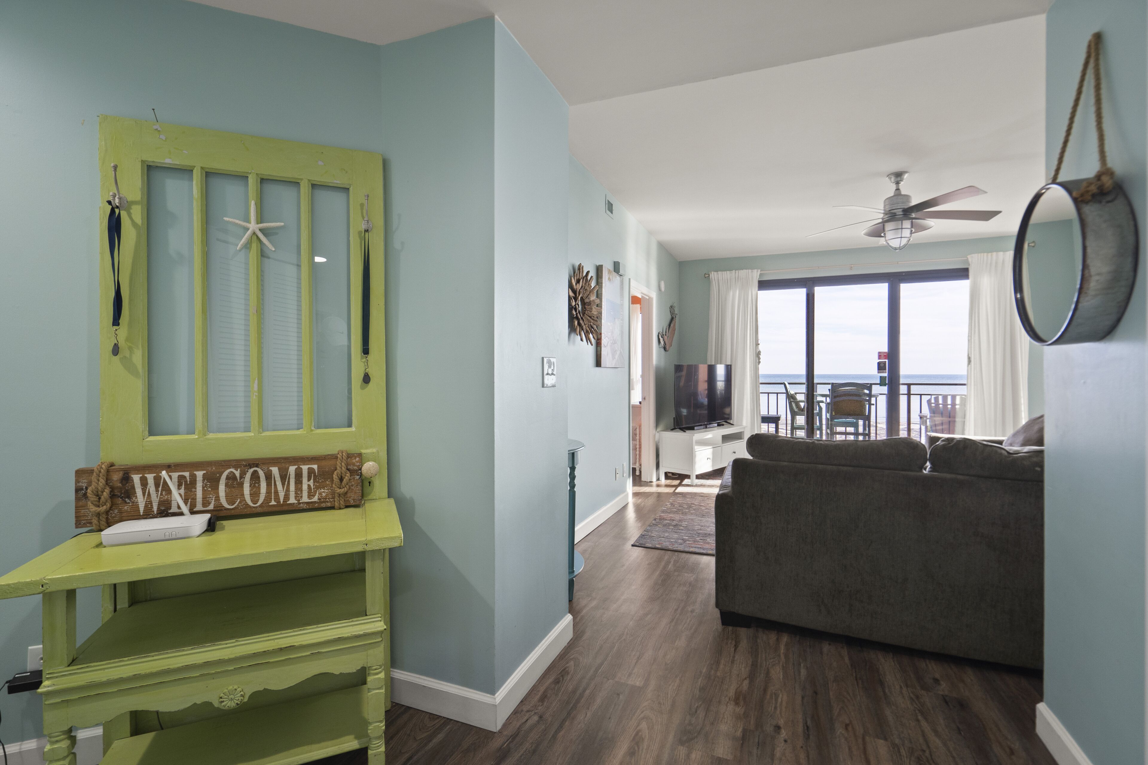A living room with a green accent wall, a gray sofa, and a balcony with a view.