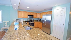 A kitchen with granite countertops, wooden cabinets, stainless steel appliances, and a white door. - Bahia Vista I 508-Baywater 10th St, Free WiFi, Pool, Elev, W/D, AC (Ocean City)