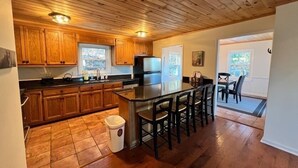 Una cocina con gabinetes de madera, encimera negra, refrigerador de acero inoxidable y una barra con taburetes.