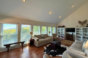 A spacious living room with a high ceiling, large windows, a fireplace, a television, and a bookshelf. - Beautiful 3 bedroom mountain home with views of Grandfather Mountain (Sugar Mountain)