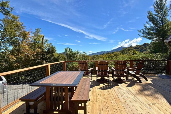 An outdoor deck with wooden furniture, including a table and chairs, overlooking a mountainous landscape.