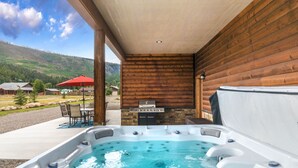 Un bain à remous avec une cheminée en pierre, des murs en bois et un espace patio aménagé avec du mobilier d’extérieur.