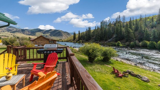 Eine Terrasse mit Adirondack-Stühlen mit Blick auf einen Fluss und Berge.