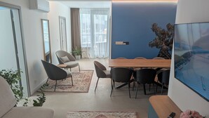 A modern living room with a dining area, a large window with curtains, a flat-screen TV, and a potted plant. - Slavic Industrial Apartment by CHORS (Bratislava)