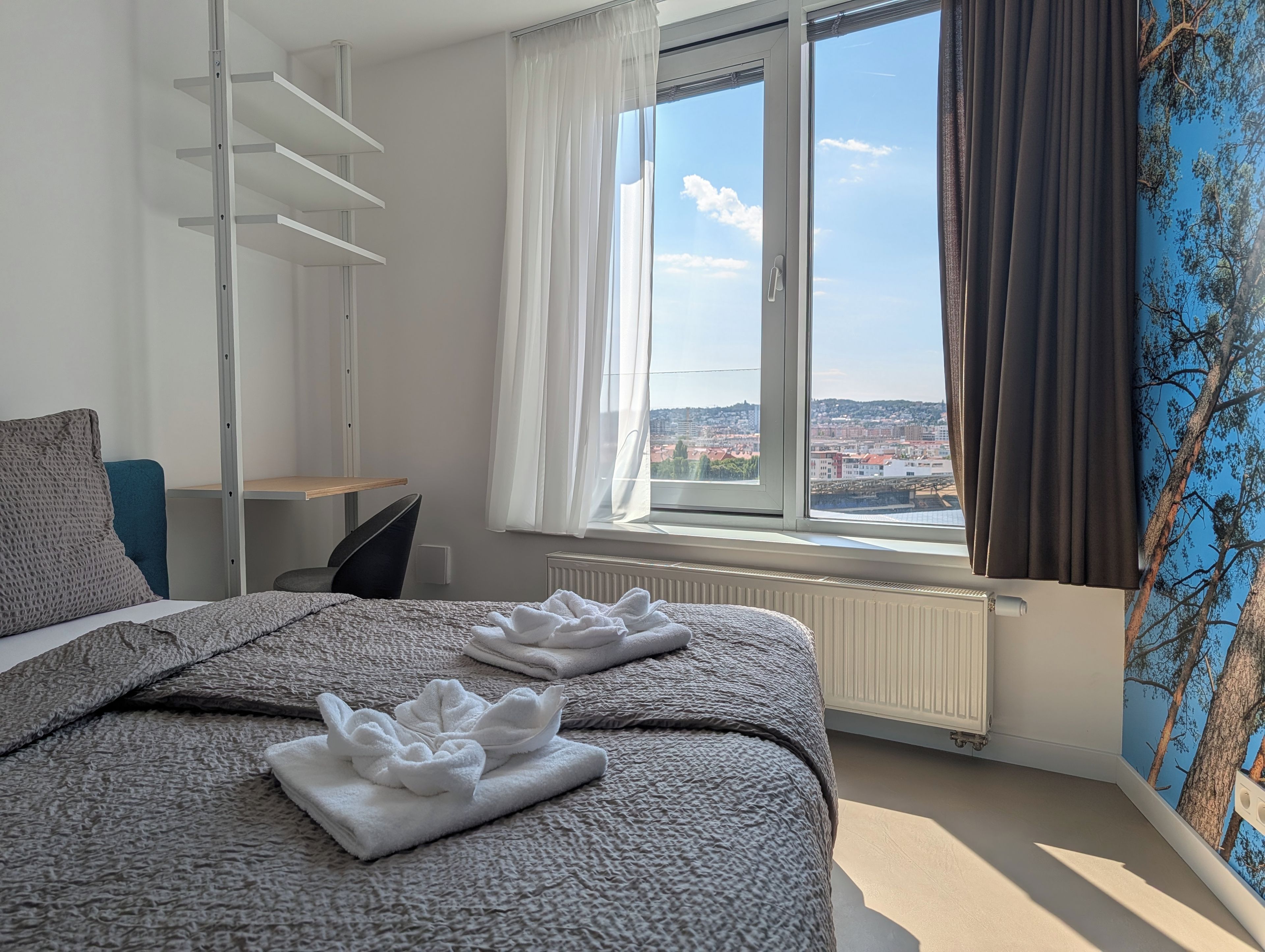 Una camera d'hotel con un letto, una scrivania, una sedia e una finestra vista città.