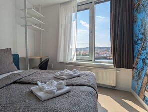 A hotel room with a bed, a desk, a chair, and a window with a city view.