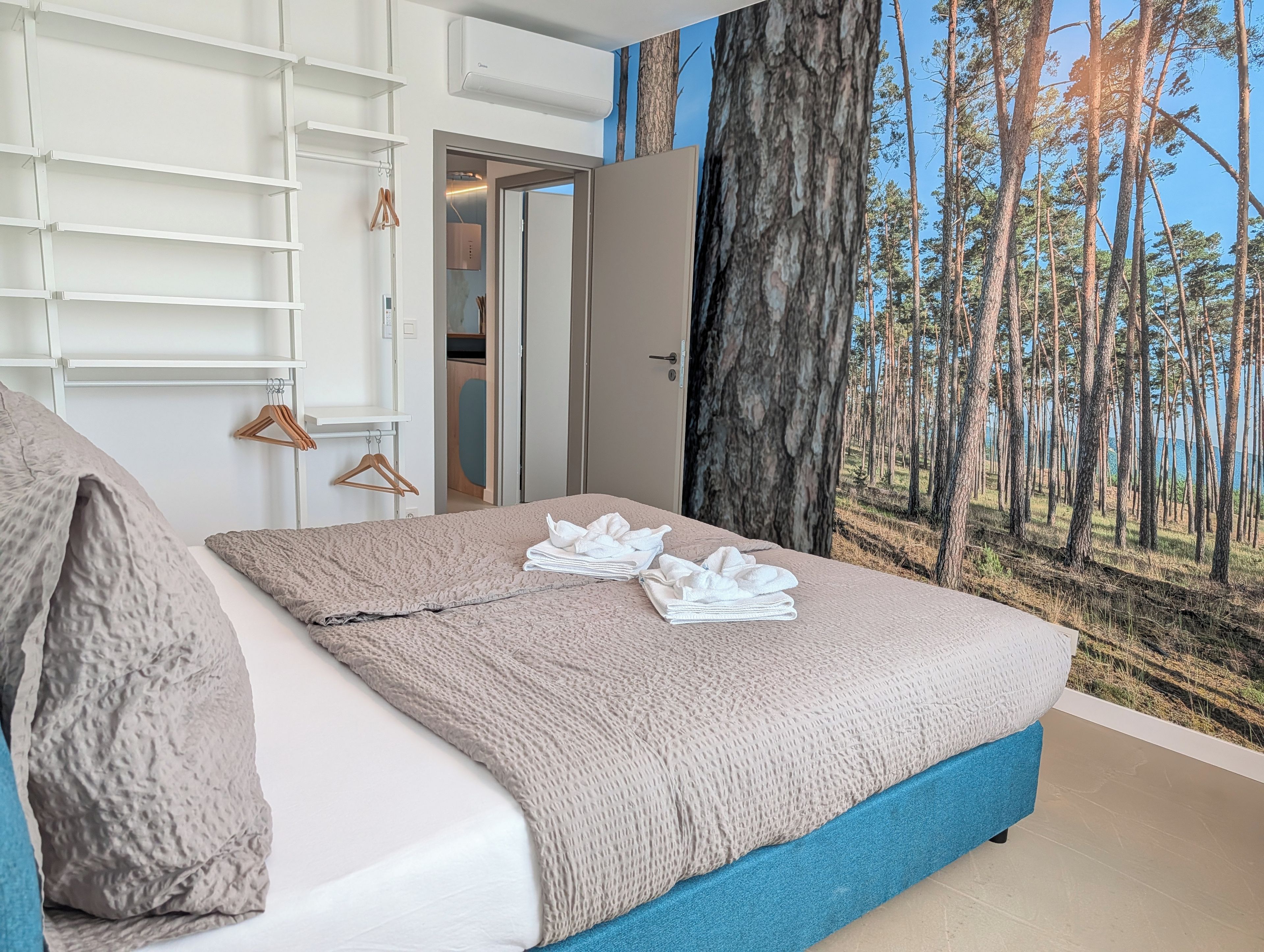 A bedroom with a bed, a wardrobe, and a large forest mural on the wall.