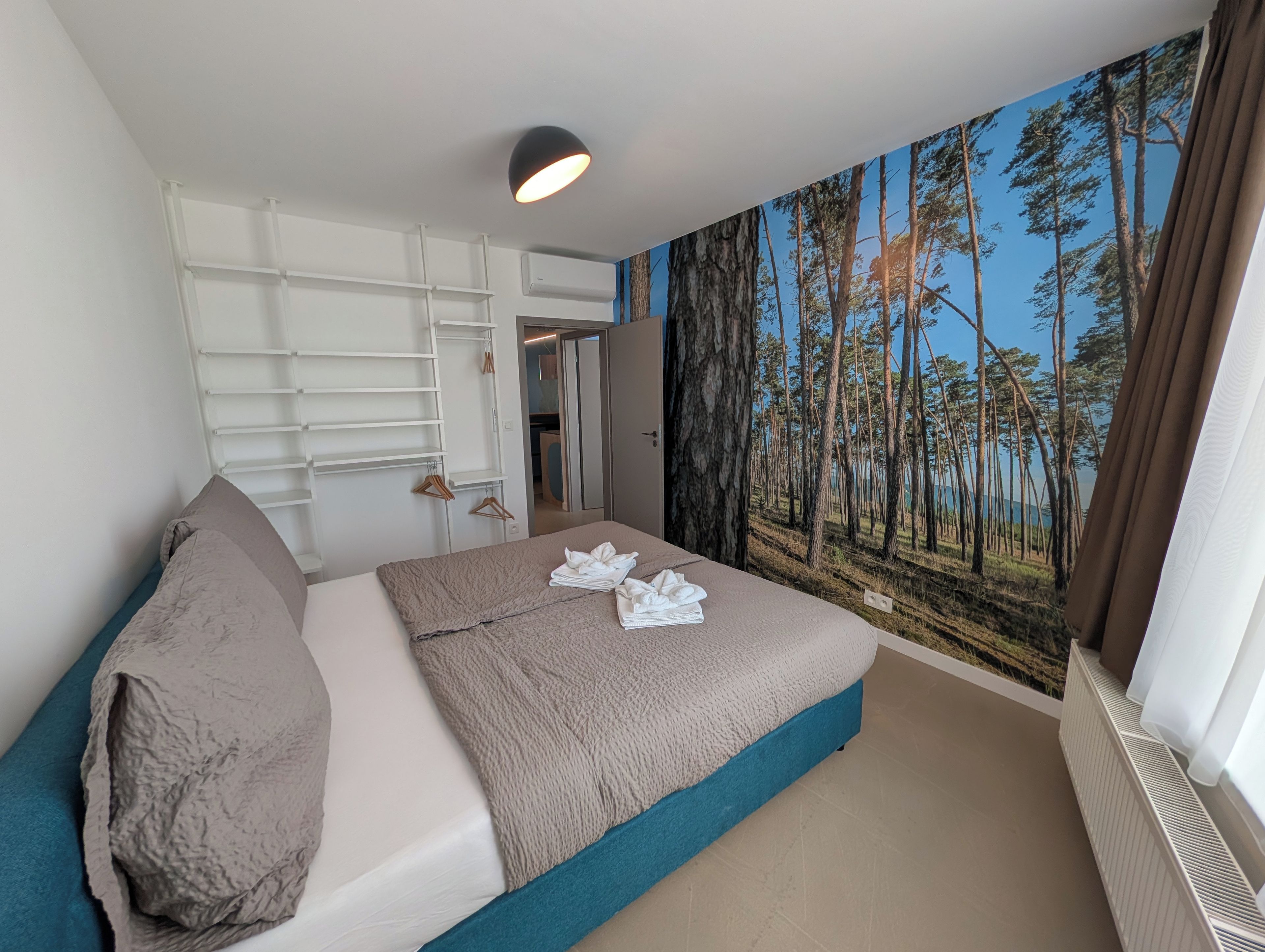 A bedroom with a bed, a wardrobe, and a mural of a forest.
