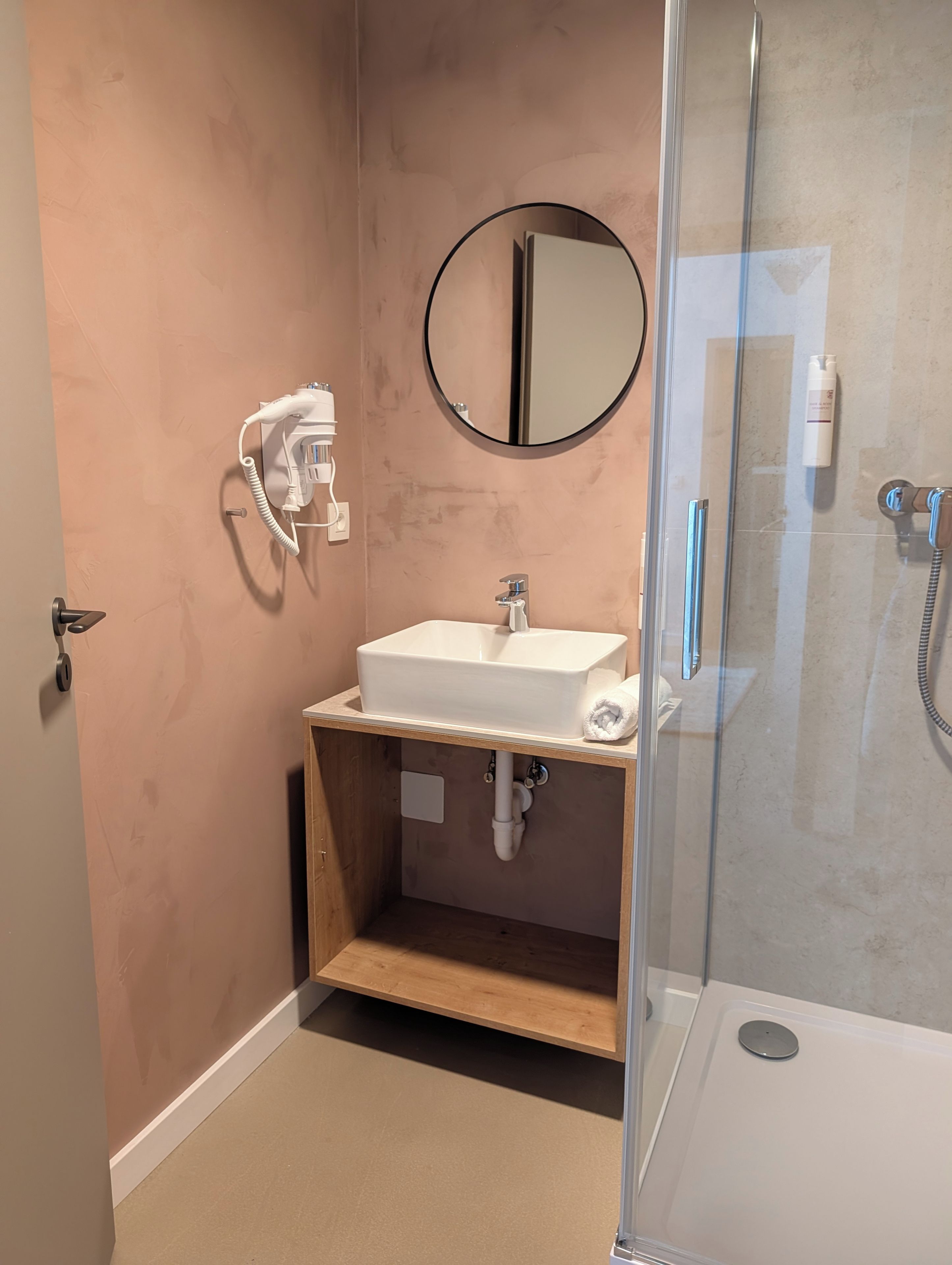 A bathroom with a white sink, a mirror, a towel, a shower, and a hairdryer.