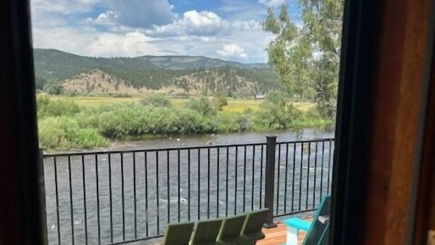 Une terrasse avec deux fauteuils Adirondack verts et une chaise longue bleue, offrant une vue sur une rivière et des montagnes.