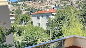 A balcony with two wooden chairs and a small table, overlooking a hillside with buildings and greenery. - Zirve Suit Rezidans (Talas)