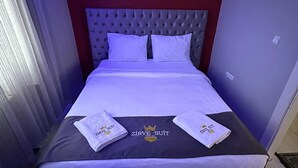 A neatly made bed with a tufted headboard, two pillows, and two towels with a logo. - Zirve Suit Rezidans (Talas)