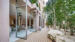 A modern building with large glass doors, a wooden deck, and a garden area with rocks and trees. - Stunning Studio Tulum Jungle w/ Pool Restaurant (Tulum)