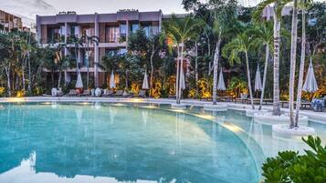 Una piscina rodeada de sillas de descanso y sombrillas, con un edificio al fondo.