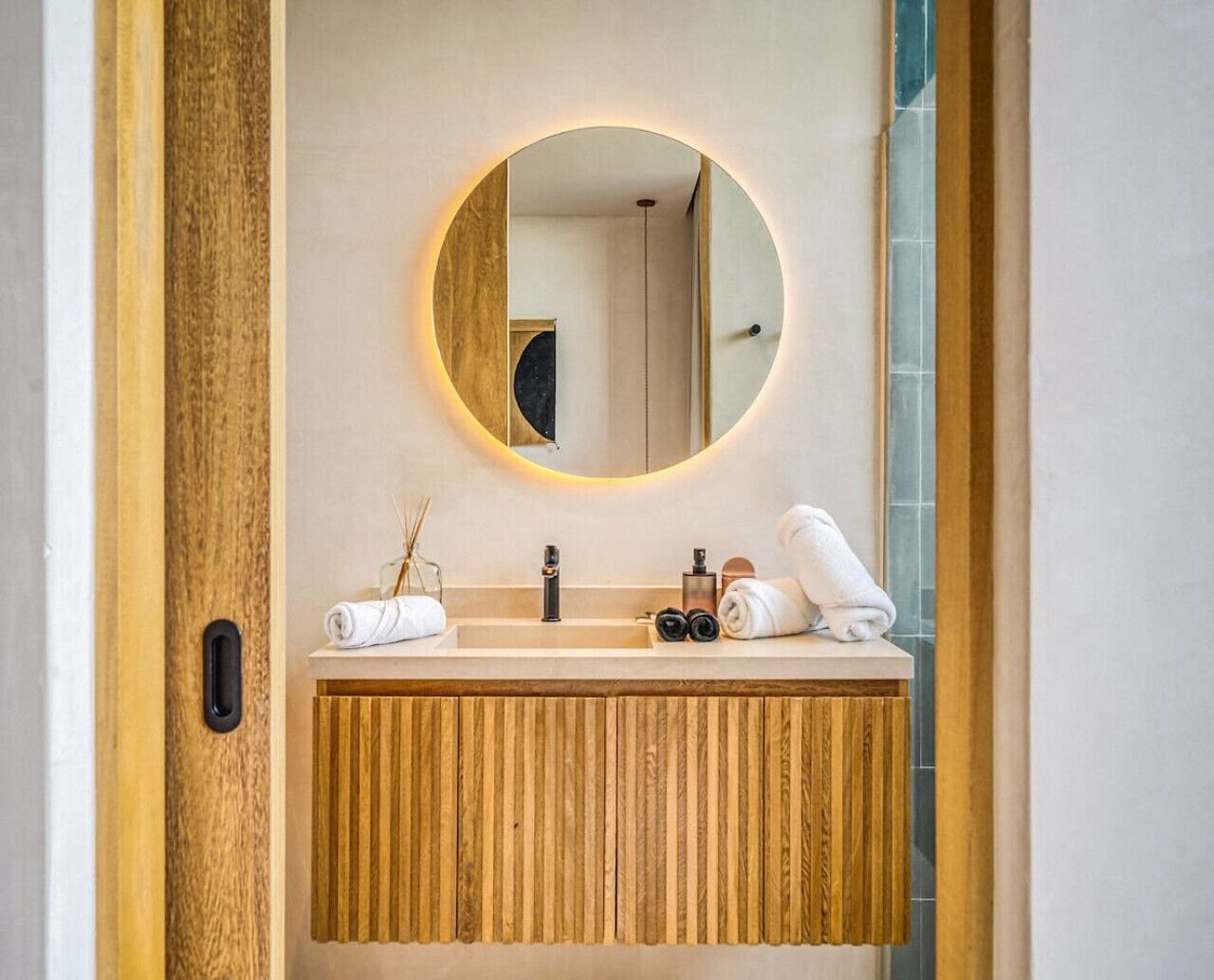 Une salle de bain avec un meuble-lavabo en bois, un miroir rond avec un éclairage intégré et deux vasques.