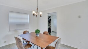 A dining room with a wooden table, six chairs, a chandelier, a potted plant, and a view of a laundry room. - Residency Savannah  (Savannah)