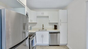 A compact kitchen with white cabinetry, a stainless steel refrigerator, a dishwasher, and a coffee maker on the countertop. - Residency Savannah  (Savannah)