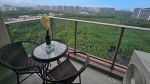 Un balcon avec des fauteuils en osier, une table en verre et un vase.