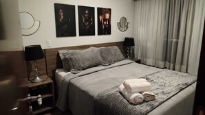 Une chambre d’hôtel avec un lit, deux lampes de chevet, une table de nuit et un mur orné de trois tableaux encadrés.