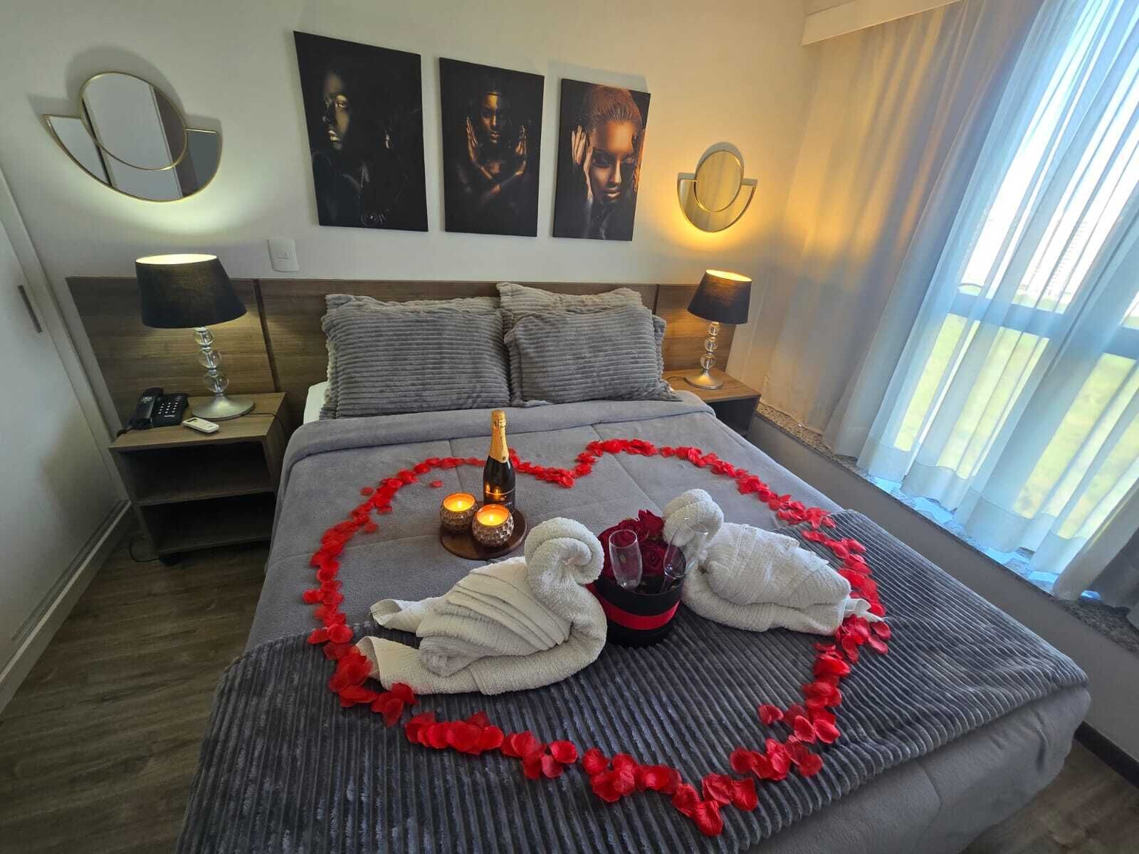 Une chambre d’hôtel avec un lit, deux tables de chevet, une commode, un mur orné de trois tableaux encadrés et une fenêtre avec des rideaux.