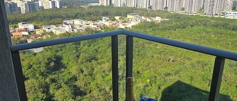 A balcony with a table set for two, overlooking a cityscape with buildings and greenery.