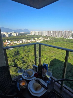 Un balcon avec une table dressée pour deux personnes, offrant une vue sur le paysage urbain, avec ses bâtiments et sa verdure.