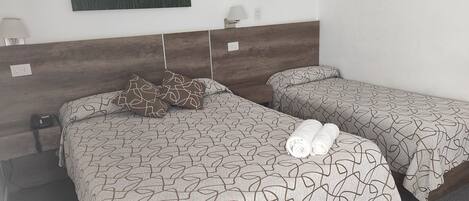 Habitación de hotel con dos camas individuales, cada una con ropa de cama y almohadas estampadas. En la pared, sobre las camas, hay un cuadro, una mesita de noche con lámpara y un enchufe.