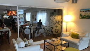 Un hall de hotel con un separador de vidrio que divide el área de comedor del área de descanso. Hay un sofá, una mesa de centro y una lámpara.