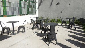 Un patio al aire libre con varias mesas y sillas, guirnaldas de luces y un edificio con un ventanal de tonos verdes.