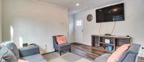 A living room with a grey sofa, a grey armchair, and a wooden entertainment unit with a flat-screen TV.