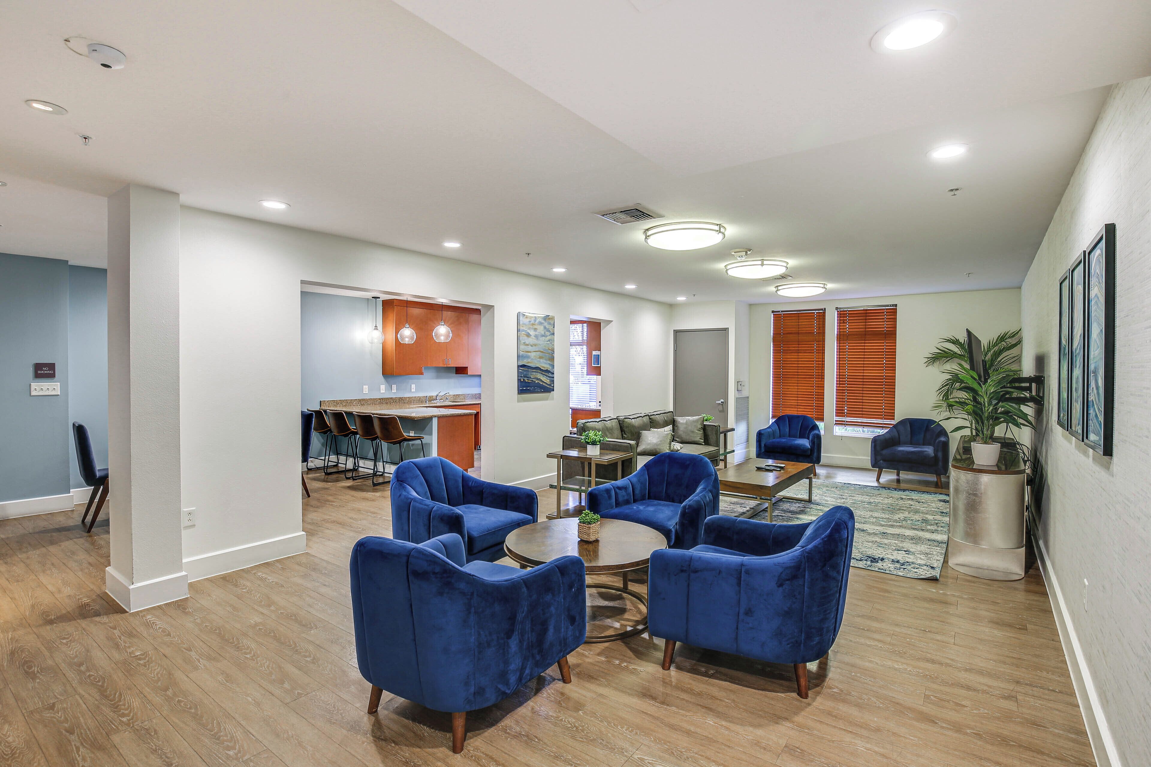 Un espacio habitable amplio, con una cocina al fondo, que incluye sillones azules y una mesa de centro.