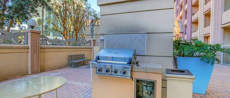 Cocina exterior con una parrilla, una mesa y un bote de basura.