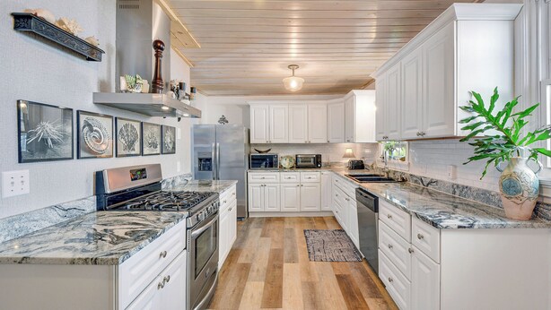 A modern kitchen with white cabinets, a marble countertop, and a wooden floor. - 0.1 Miles to Beach • Pet Friendly •  Walk to King & Prince • 2 Master Suites (St Simons Island)